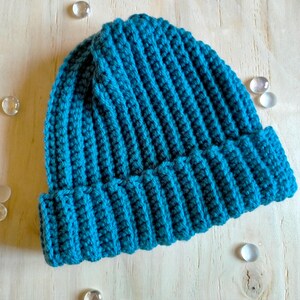 Puede incluir: Un gorro de punto de color azul turquesa. El gorro est&aacute; hecho con punto de canal&eacute; y tiene un borde doblado.