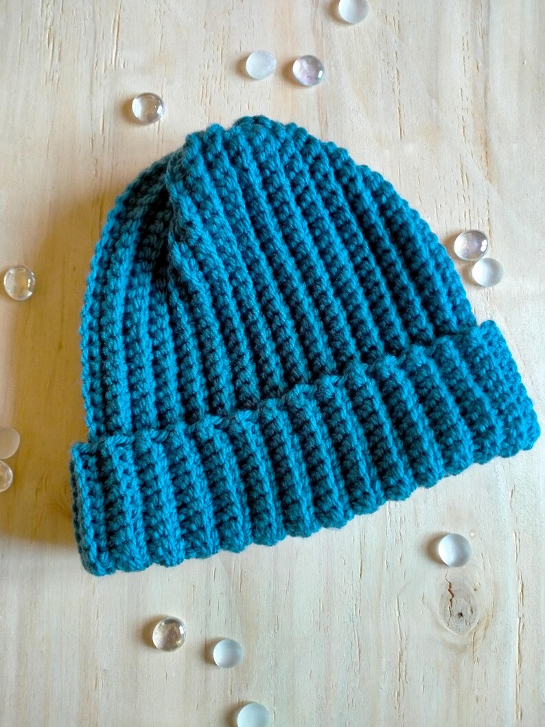 Puede incluir: Un gorro de punto de color azul turquesa. El gorro est&aacute; hecho con punto de canal&eacute; y tiene un borde doblado.