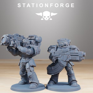 May include: Two grey miniature figurines of armoured soldiers, each holding a large weapon. The figurines are standing on circular bases. The text "STATIONFORGE" and a skull logo are visible at the top.