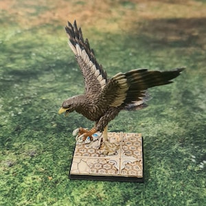 Könnte beinhalten: Eine braun und schwarz bemalte Miniatur eines Adlers mit ausgebreiteten Flügeln, die auf einem quadratischen Sockel mit einem beige-braunen Wabenmuster sitzt.