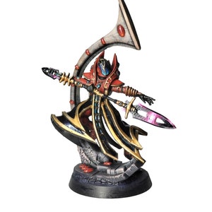 May include: A red and gold painted miniature figurine of a warrior holding a spear and standing on a black base. The warrior is wearing a black and gold robe and has a large, white horn behind it.