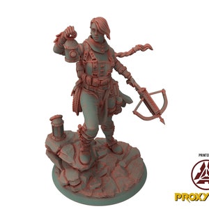 Peut inclure: Une miniature imprimée en 3D d'une femme tenant une lanterne et une arbalète. Elle porte une veste en cuir et un pantalon, et a une longue tresse. La miniature est debout sur une base rocheuse.