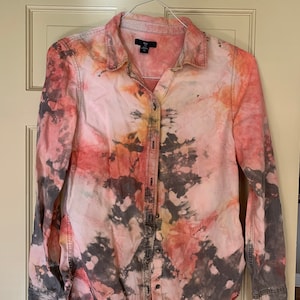 Puede incluir: Una camisa de manga larga con botones y un estampado tie-dye en tonos rosa, naranja, amarillo y negro.