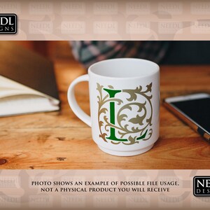 May include: A white ceramic mug with a green and gold letter L design. The mug is sitting on a wooden table with a notebook and a cell phone.