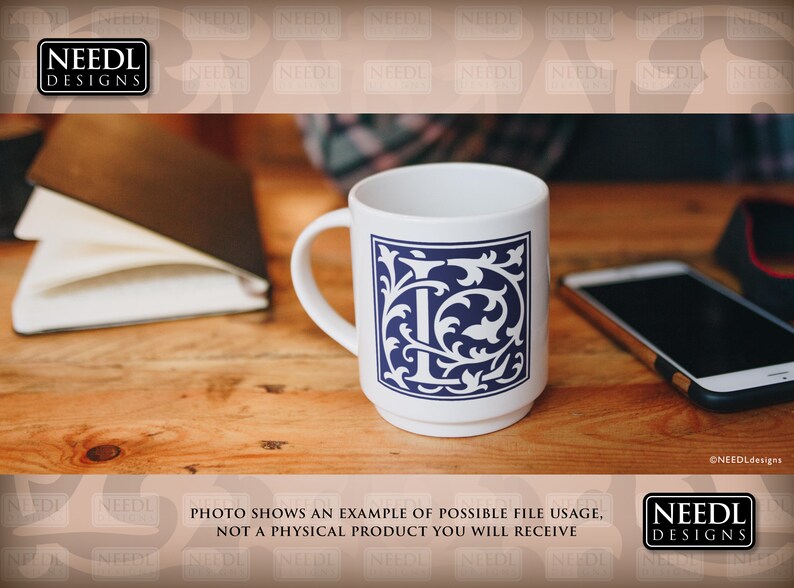 May include: White ceramic mug with a blue and white floral design featuring the letter "I" in the center. The mug is on a wooden table with a notebook and a cell phone.