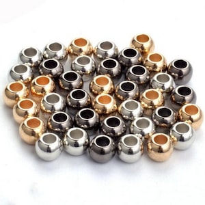 May include: A collection of round metal beads in gold, silver, and black.