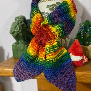 Könnte beinhalten: Ein gestrickter Schal in Regenbogenfarben mit einem Farbmuster in Lila, Blau, Grün, Gelb, Orange und Rot.