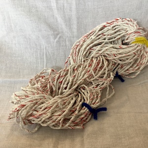 May include: A large bundle of white cotton mop strings with red stripes. The strings are tied together with a yellow rubber band and blue pipe cleaners.