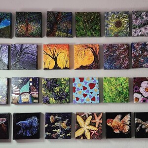 May include: A wall gallery of 24 small square paintings. The paintings feature a variety of subjects, including landscapes, flowers, animals, and abstract designs. The paintings are all framed in black and are arranged in a grid pattern.