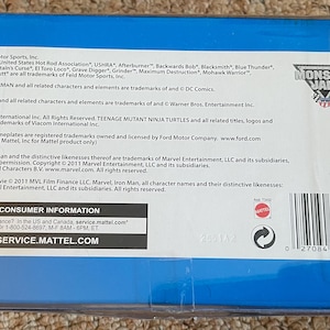 May include: A blue box with text including "Monster Jam" logo and various trademarks. The box contains consumer information and a barcode. The text mentions "Batman", "Superman", "Looney Tunes", and "Teenage Mutant Ninja Turtles".