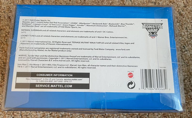 May include: A blue box with text including "Monster Jam" logo and various trademarks. The box contains consumer information and a barcode. The text mentions "Batman", "Superman", "Looney Tunes", and "Teenage Mutant Ninja Turtles".
