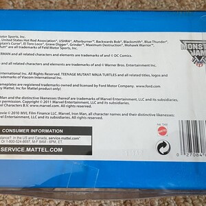 K&ouml;nnte beinhalten: Eine blaue Box mit Text, darunter "Monster Jam" und "Consumer Information". Die Box enth&auml;lt auch Logos f&uuml;r "Monster Jam" und Mattel. Der Text listet Marken und Urheberrechtsinformationen f&uuml;r verschiedene Marken auf.
