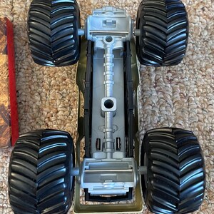 May include: A toy monster truck with four large black tires and a gray chassis. The truck has a detailed undercarriage and is designed for off-road play. The tires have a deep tread pattern for traction.
