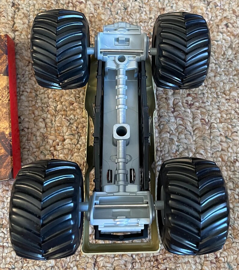 May include: A toy monster truck with four large black tires and a gray chassis. The truck has a detailed undercarriage and is designed for off-road play. The tires have a deep tread pattern for traction.