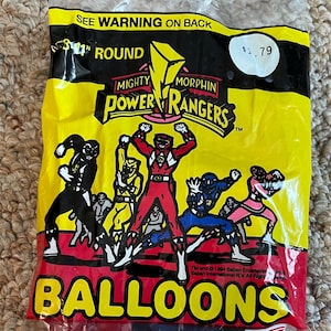 May include: Sealed package of Mighty Morphin Power Rangers balloons. The package is yellow and red, with the Power Rangers logo and characters. The balloons are 11 inches round and made in the USA.