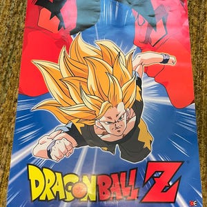 Könnte beinhalten: Ein Dragon Ball Z-Poster mit einer dynamischen Illustration eines Charakters mit stacheligen gelben Haaren und einem schwarz-goldenen Outfit vor blauem Hintergrund. Das Poster enthält das Dragon Ball Z-Logo in Gelb und Rot.
