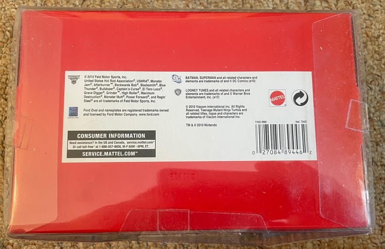 May include: A red box with a clear plastic cover. The box contains text from Feld Motor Sports, Looney Tunes, and Mattel. The box also has a barcode and the text "CONSUMER INFORMATION" and "SERVICE.MATTEL.COM".