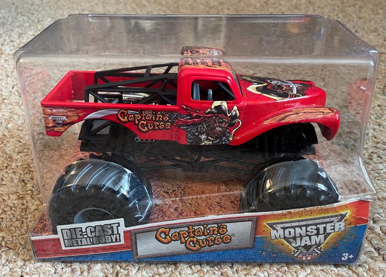 May include: A red die-cast metal body monster truck toy, "Captain's Curse", in a clear plastic package. The truck has large black tires and a black roll cage. The package features the Monster Jam logo.