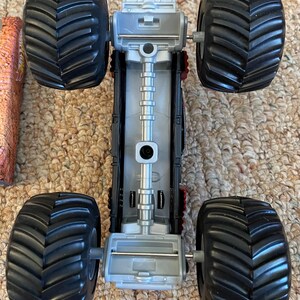 May include: A toy monster truck with large black tires and a silver and black chassis. The tires have a deep tread pattern. The truck's body has red accents and a detailed design.
