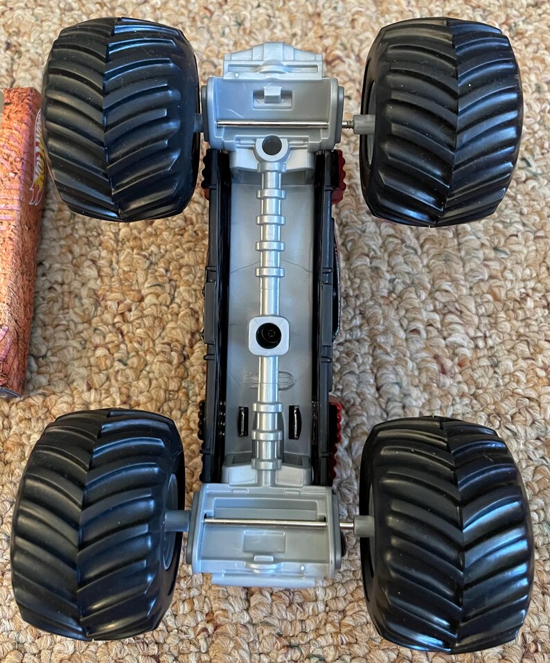 May include: A toy monster truck with large black tires and a silver and black chassis. The tires have a deep tread pattern. The truck's body has red accents and a detailed design.