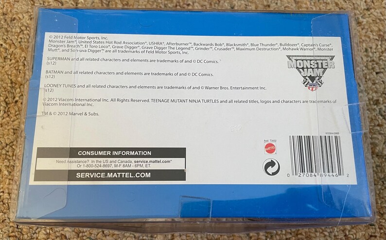 May include: A blue box with the Monster Jam logo and text. The box contains information about trademarks and consumer information. The box has a barcode and the text "SERVICE.MATTEL.COM".