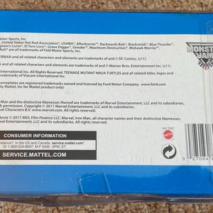 May include: A blue box with text and logos, including "Monster Jam." The box contains information about trademarks and licensing for various brands, including Marvel, DC Comics, and Ford. The box also includes consumer information.