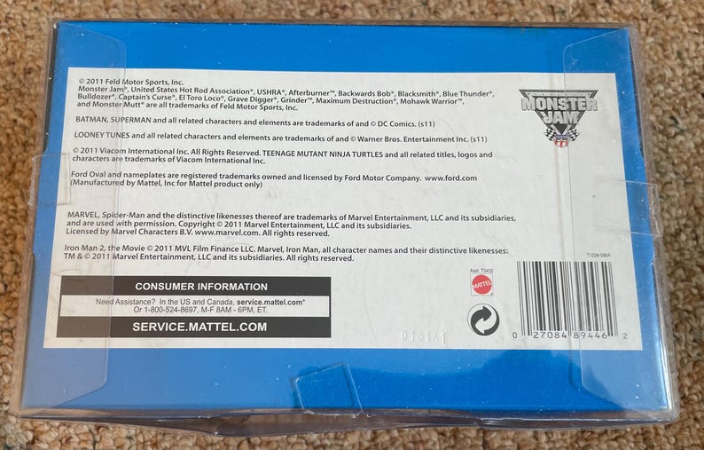 May include: A blue box with text and logos, including "Monster Jam." The box contains information about trademarks and licensing for various brands, including Marvel, DC Comics, and Ford. The box also includes consumer information.