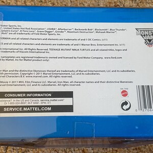 May include: A blue box with a white label featuring text about Monster Jam, DC Comics, and Marvel characters. The box includes a barcode and the Monster Jam logo.