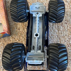 May include: A blue and silver toy monster truck with large black tyres. The truck has a detailed chassis and is designed for off-road play. The tyres are approximately 10 cm in diameter.