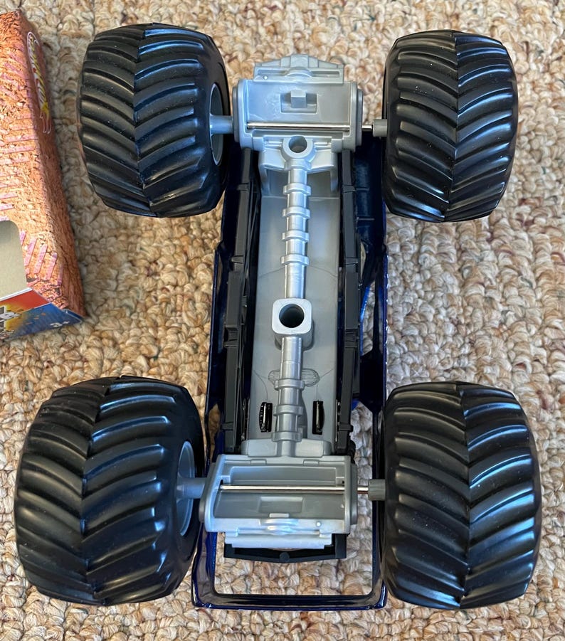 May include: A blue and silver toy monster truck with large black tyres. The truck has a detailed chassis and is designed for off-road play. The tyres are approximately 10 cm in diameter.