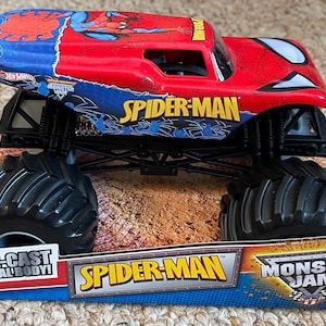 May include: A red and blue Spider-Man monster truck toy with black tires. The truck has the words "Spider-Man" and "Monster Jam" on it. The toy is on a cardboard display.
