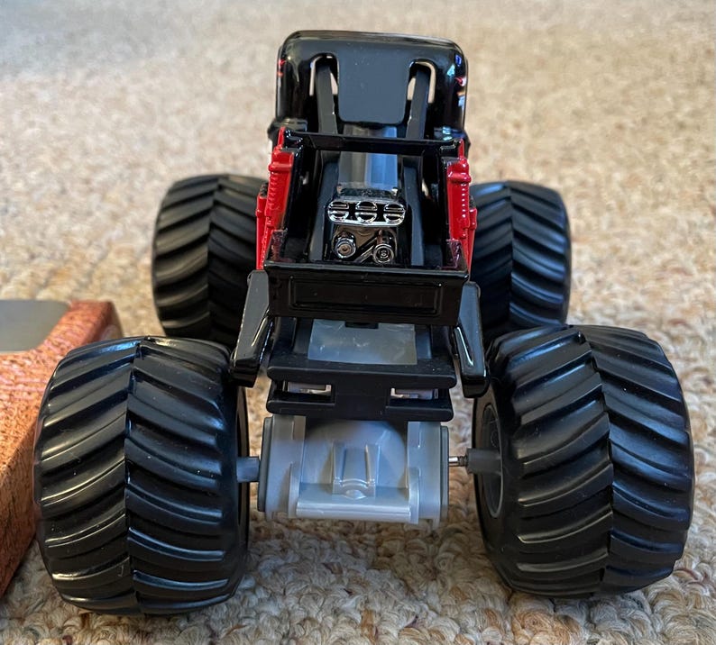 May include: A black and red toy monster truck with large, black tires. The truck has a detailed engine and suspension system. The tires are thick and have deep treads. The truck is designed to look like a real monster truck.