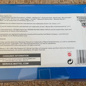 May include: A blue plastic package with text and logos for Monster Jam, including trademarks for various characters and companies. The package includes a barcode and consumer information.
