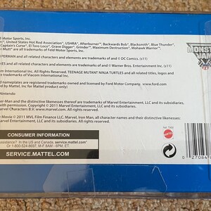 May include: A blue and white box with the Monster Jam logo. The box contains text about trademarks and consumer information. The text includes the names of Monster Jam, Batman, Superman, Looney Tunes, Teenage Mutant Ninja Turtles, and Marvel characters.