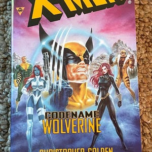 Puede incluir: Portada de cómic de "X-Men: Codename Wolverine" de Christopher Golden. La portada presenta a Wolverine con sus garras extendidas y otros personajes de X-Men. El título es amarillo, con un fondo morado y rosa.