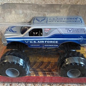 Pu&ograve; includere: Un camion mostro giocattolo della U.S. Air Force argento e blu in una confezione di plastica trasparente. Il camion presenta grandi pneumatici neri e le parole "U.S. AIR FORCE" e "AFTERBURNER" stampate sui lati.
