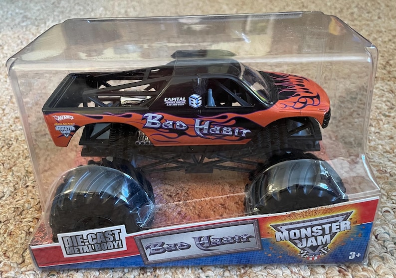 May include: Die-cast metal body monster truck toy in a clear plastic package. The truck is orange and black with the words "Bad Habit" and flame graphics. The package also features the Monster Jam logo.