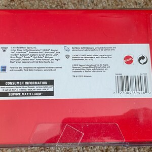 Puede incluir: Una caja roja con una cubierta de pl&aacute;stico transparente. La caja contiene texto, incluyendo "CONSUMER INFORMATION" y "SERVICE.MATTEL.COM". La caja tambi&eacute;n tiene un c&oacute;digo de barras y el logotipo de Mattel.