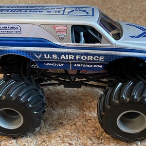 Pu&ograve; includere: Un camion mostro giocattolo della U.S. Air Force argento e blu con grandi pneumatici neri. Il camion presenta la scritta "U.S. AIR FORCE" e "AFTERBURNER". Il logo Hot Wheels &egrave; visibile.