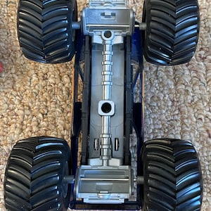 May include: A toy monster truck with four large black tires and a blue and silver chassis. The truck has a detailed undercarriage and is designed for off-road play. The tires have a deep tread pattern for traction.