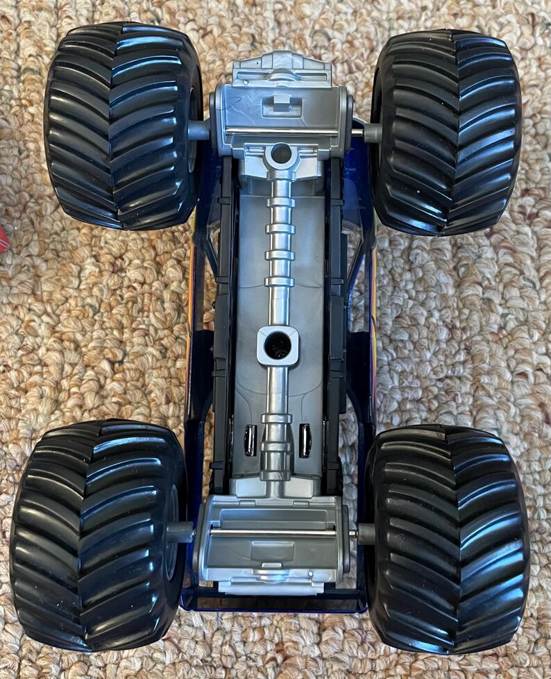 May include: A toy monster truck with four large black tires and a blue and silver chassis. The truck has a detailed undercarriage and is designed for off-road play. The tires have a deep tread pattern for traction.