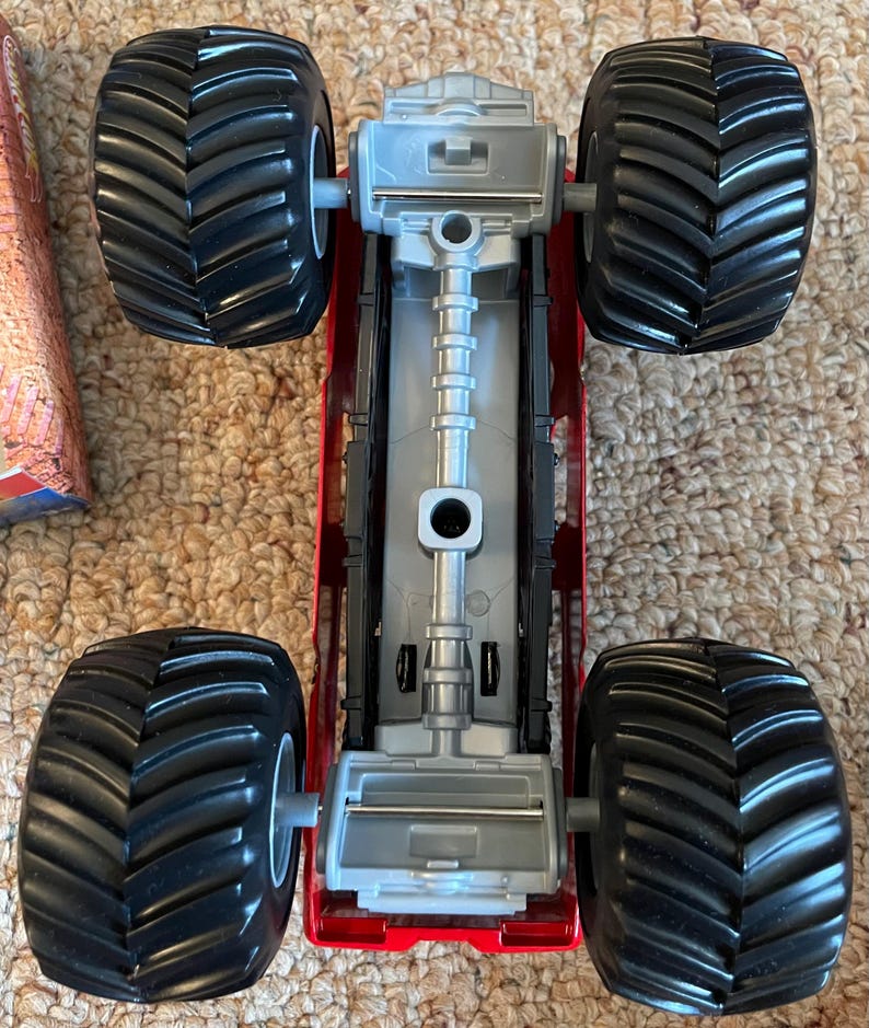 May include: A red and silver toy monster truck with four large black tires. The truck has a detailed chassis and is designed for off-road play. The tires have deep treads for traction.