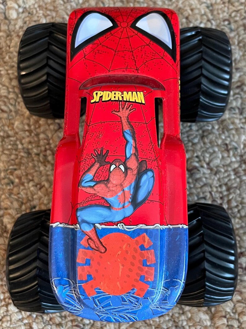 May include: A red and blue Spider-Man monster truck toy with large black tires. The truck features the Spider-Man logo and a graphic of Spider-Man. The toy is designed for play and display.