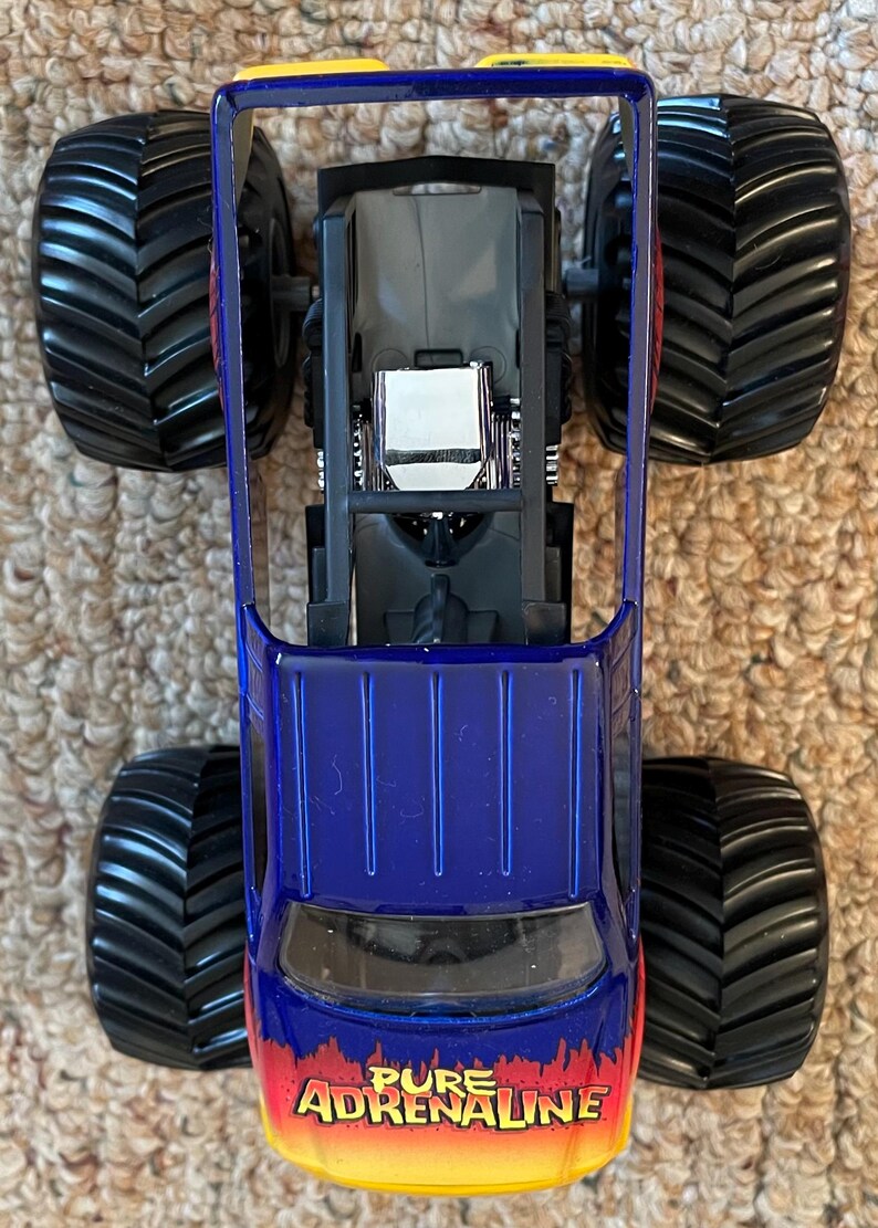 Może przedstawiać: Niebiesko-ż&oacute;łta zabawka monster truck z dużymi czarnymi oponami. Na przodzie ciężar&oacute;wki widnieje napis "PURE ADRENALINE". Widok ciężar&oacute;wki z g&oacute;ry.
