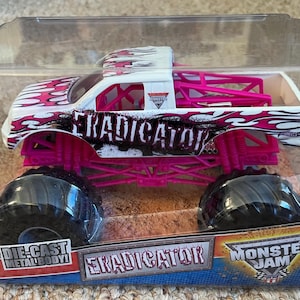 May include: Die-cast metal body toy monster truck, the "Eradicator", in a clear plastic package. The truck is white with pink and black flame graphics, pink chassis, and large black tires. The text "Eradicator" is visible on the side.
