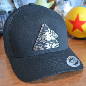 May include: Black mesh trucker hat with a silver triangle patch featuring a spaceship and the text "FLY CASUAL".