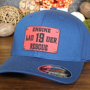 May include: A navy blue Flexfit baseball cap with a red rectangular patch. The patch features the words "ENGINE LAD 19 DER RESCUE" in black lettering. The cap has a curved brim and a Flexfit label.
