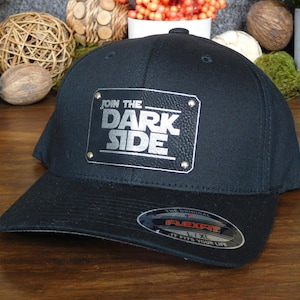 May include: Black Flexfit baseball cap with a silver metallic patch that reads "JOIN THE DARK SIDE." The hat has a curved brim and a Flexfit sticker. A stylish accessory for fans of a popular science fiction franchise.