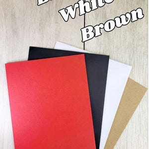 Op de afbeelding: Een selectie van gekleurde enveloppen in rood, zwart, wit en bruin, gerangschikt op een houten oppervlak. De tekst in de afbeelding luidt "Red, Black, White, Brown" en "Choose Your Envelope Color."