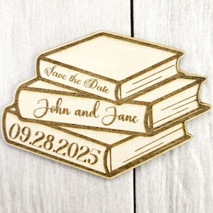 May include: A wooden save the date magnet with a stack of books. The magnet is engraved with the text "Save the Date", "John and Jane", and "09.28.2025".